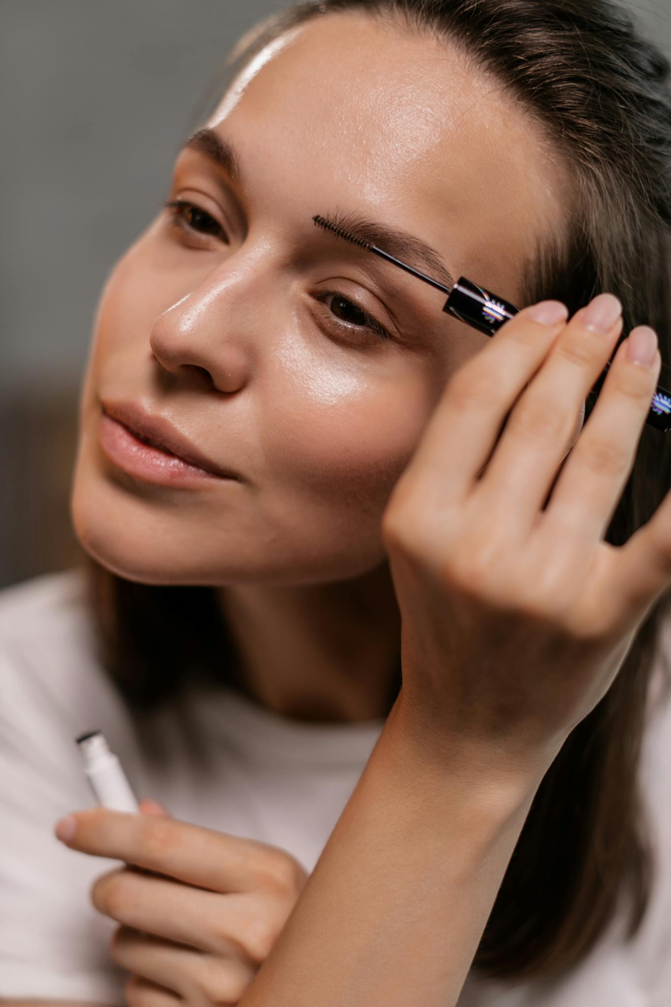 A woman in close-up applying eyebrow makeup, emphasizing natural beauty and skincare.