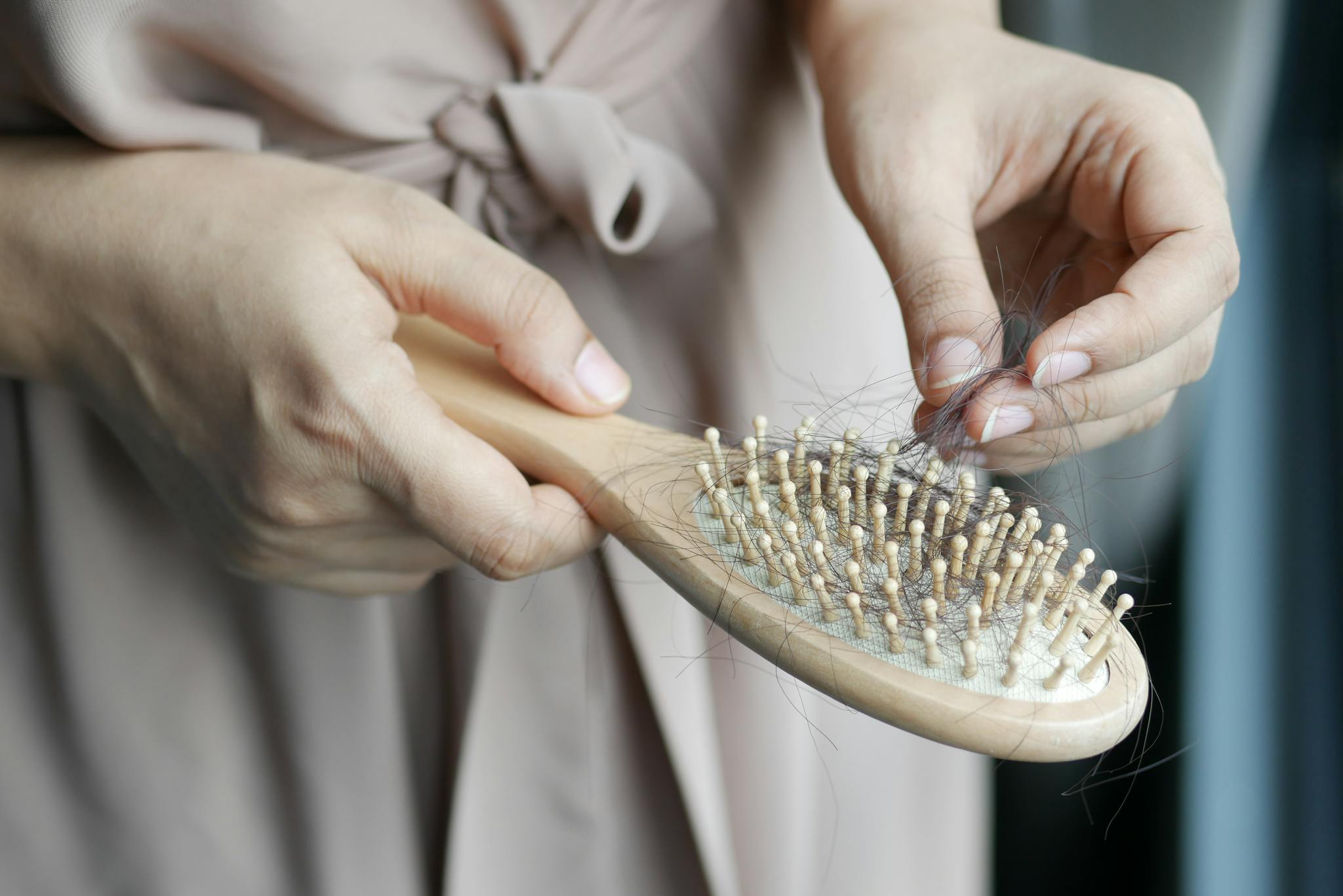 Close-up image of hands removing hair from a wooden brush, emphasizing daily hair care routine.