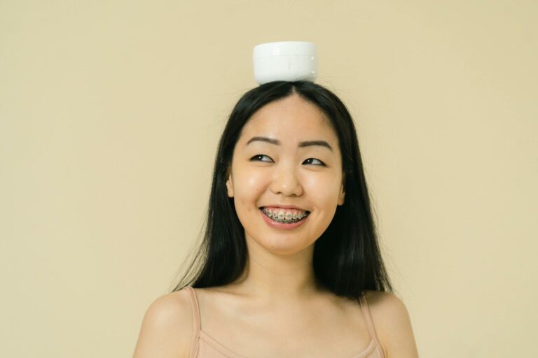 Smiling woman balancing a skincare jar on her head, captured in a studio setting.