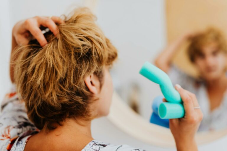 Woman using blue curlers in front of a mirror for daily hair routine.